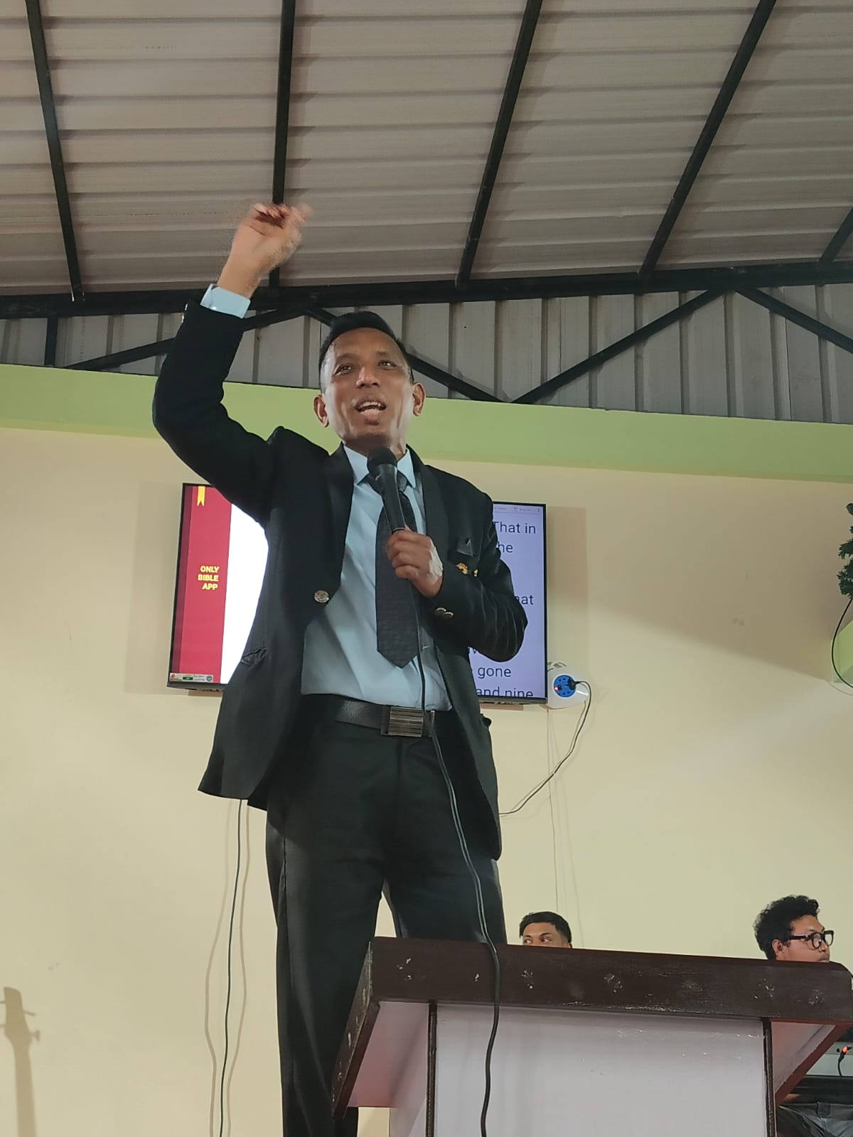 Preaching from the pulpit with arm raised.